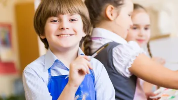 Junge lächelt und hält einen Pinsel in einem Klassenraum.