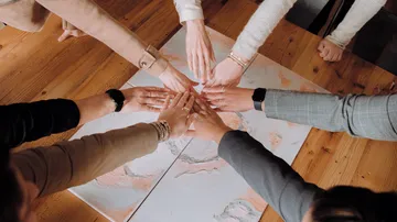 Hands touch a table with colored paper in the middle.
