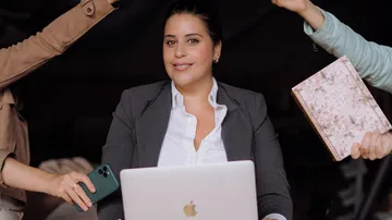Woman sitting at a computer while hands show activity.