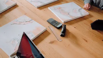 Vier Leinwände liegen auf einem Tisch, mit Schreibutensilien.