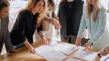 Fünf Frauen analysieren Kunstwerke an einem Holztisch.
