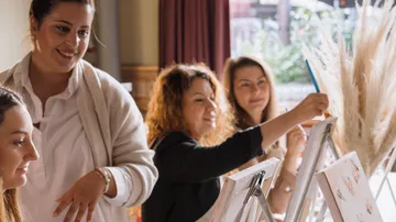 Drei Frauen malen an Staffeleien in einem hellen Raum.