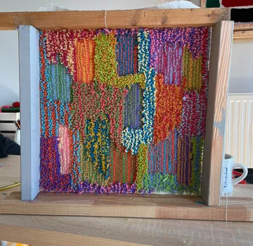 Wandbehang zeigt bunten, strukturierten Stoff auf Holzrahmen.