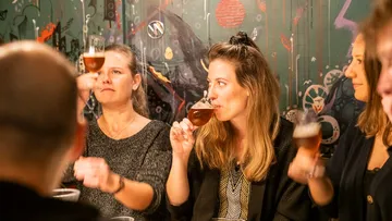 Freunde stoßen mit Biergläsern in lebhaftem Umfeld an.