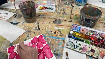 Pinsel malt rosa Formen auf Papier, umgeben von Farben.