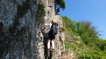 Bergsteiger klettert an Felswand auf einen hohen Pfad.