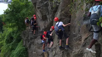 Kletternde Personen an einer steilen Felswand mit Helmen.
