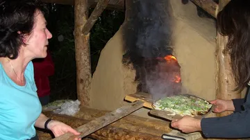 Two people bake pizza in an outdoor wood oven.