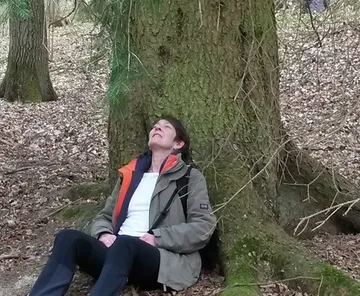 Person lehnt entspannt an einem Baum im Wald.