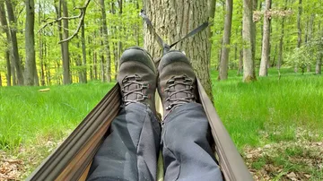 Feet rest in a hammock in the green forest.