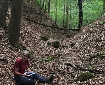 A person is sitting on the ground in the forest and working.