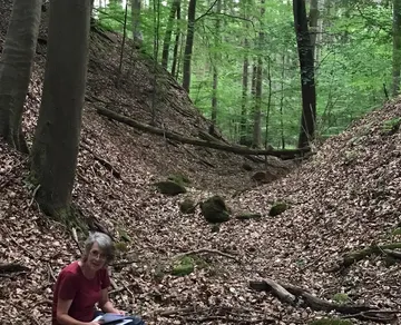 Frau sitzt im Wald und hält Papiere in der Hand.
