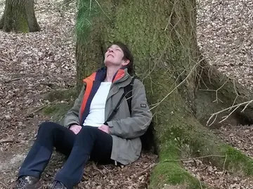 Person sitzt an Baum, blickt nach oben, entspannte Atmosphäre.