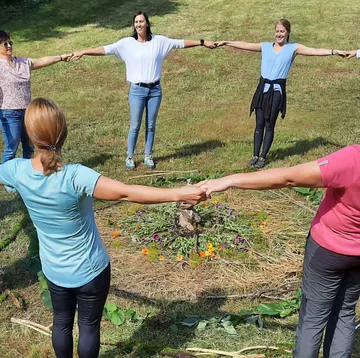 Sechs Menschen halten Hände in einem Kreis auf Wiese.