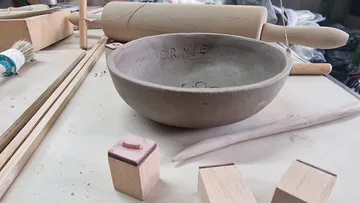 Eine Schüssel aus Ton liegt auf einem Tisch, umgeben von Werkzeugen.
