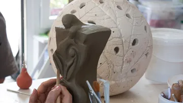Tonfigur wird mit einem Werkzeug bearbeitet, in einem Atelier.