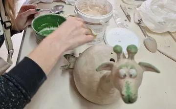 Eine Töpferfigur wird mit Farbe bearbeitet. Sie zeigt ein Tier.