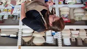 Frau malt im Atelier, umgeben von Materialien und Werkzeugen.