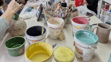 Töpferwerkzeug und Farben auf einem Tisch, jemand arbeitet daran.