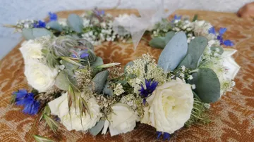 Blumenkranz aus weißen und blauen Blumen auf Tisch.