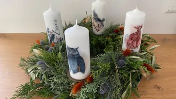 Kerzen mit Tiermotiven stehen auf einem grünen Adventskranz.