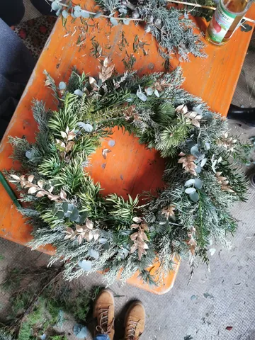 A wreath of greens is lying on a wooden table.