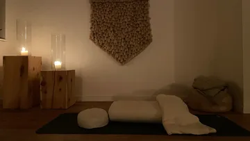 Yoga-Matte mit Kissen, Kerzen brennen in dunkler Umgebung.