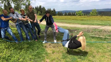 Six people pull a rope while one person hangs.