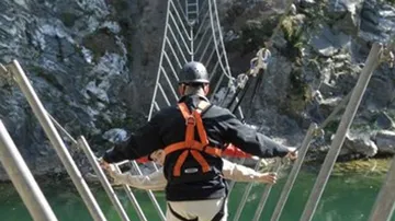 People cross a swinging suspension bridge over water.