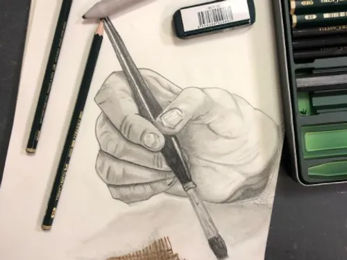 Hand holds brush, draws on paper surrounded by pens.