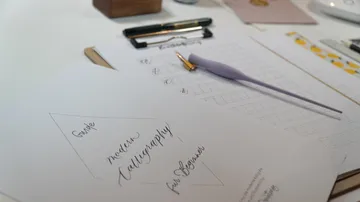 Papier mit Calligraphie-Anleitung auf einem Tisch.