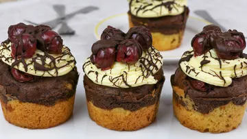 Drei Muffins mit Schokoladenglasur und Kirschen dekoriert.