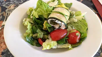 Zucchini-Rolle liegt auf buntem Salat mit Kirschtomaten.