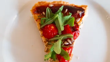 A piece of quiche with spinach and cherry tomatoes is on a plate.