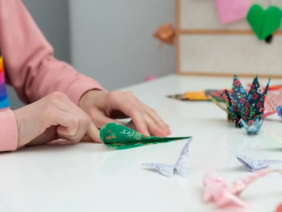 A person folds green paper into an origami crane shape.