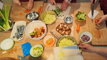Slicing vegetables at the table, several hands and ingredients visible.