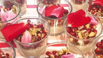 Glasses with desserts decorated with pomegranates and flower petals.