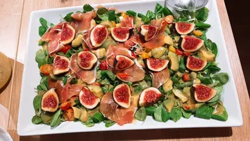 Salad with figs and ham on white plate.
