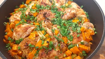 Chicken pieces with pumpkin and green onions in a pan.