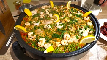 Cook large paella, decorated with shrimp and lemon.