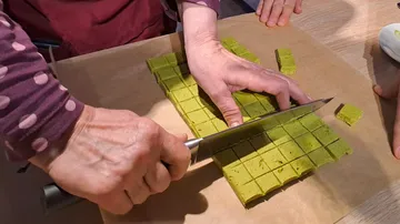 Hands cut green candy on wooden base in kitchen.