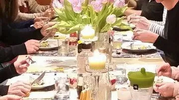 Tischgedeck mit Blumen, Kerzen und Menschen beim Essen.