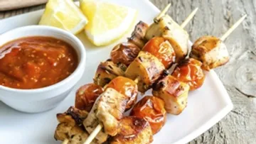 Spieße mit gegrilltem Hähnchen und Kirschtomaten, serviert.