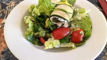 Mixed salad with stuffed zucchini roll on plate.