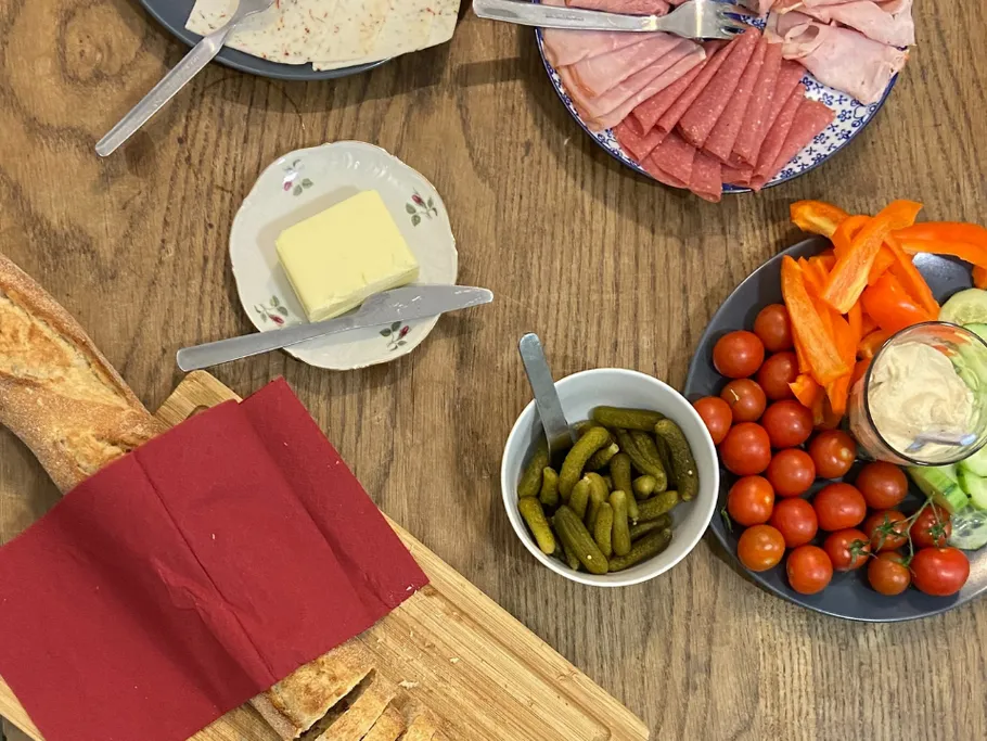 Brot, Wurst und Gemüse auf einem Holztisch angerichtet.