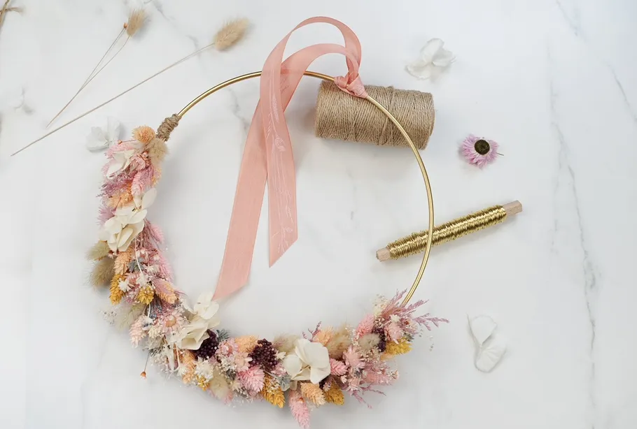 Blumenkranz auf Tisch, umgeben von Bastelmaterialien.