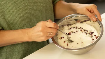 A person stirs in a bowl with sugar and flowers.
