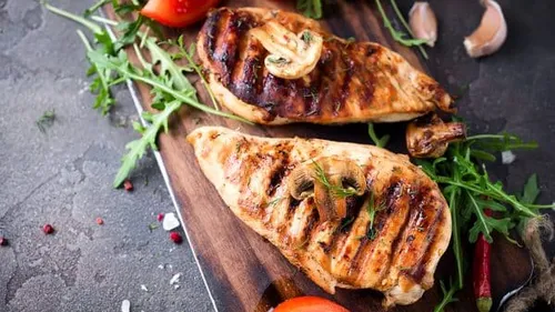Gegrilltes Hähnchen auf einem Holzbrett mit Gemüse.