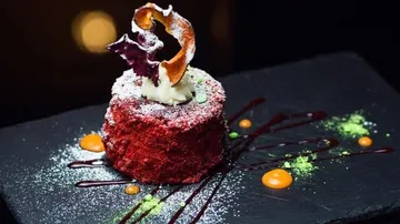 Kuchenstück dekoriert mit Sahne und Soße auf schwarzem Teller.
