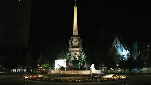 Ein Obelisk steht nachts umgeben von einem Brunnen.